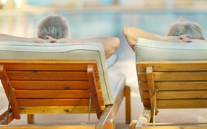 lifestyle image of a couple laying on reclining chairs beside a pool